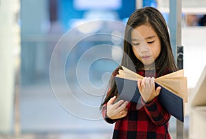 Portrait Asian child holding open textbook in hands in book store