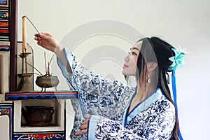 Portrait of Asian Chinese girl in traditional dress, wear blue and white porcelain style Hanfu, Light the candles on the stove