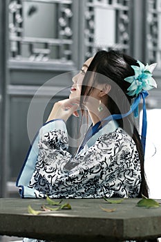 Portrait of Asian Chinese girl in traditional dress, wear blue and white porcelain style Hanfu, sit on a stone chair