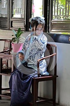 Portrait of Asian Chinese girl in traditional dress, wear blue and white porcelain style Hanfu, sit on a wooden chair