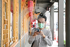 Portrait of Asian Chinese man wearing surgical face mask and texting on his cell phone