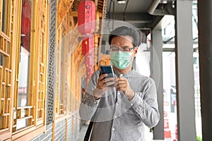 Portrait of Asian Chinese man wearing surgical face mask and texting on his cell phone