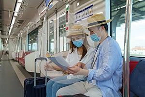 Portrait of Asian couple tourists with mask standing and holding the paper metro map together in the Skytrain in Bangkok, Thailand