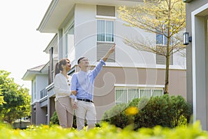 Portrait of Asian couple walking hugging and pointing together looking happy in front of their new house to start new life. Family