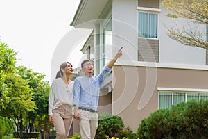 Portrait of Asian couple walking and hugging together looking happy in front of their new house to start new life. Family, age,
