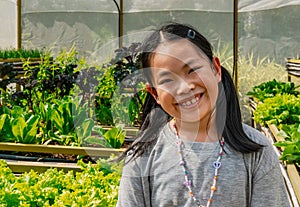 Portrait of Asian cute child girl in an organic vegetable greenhouse, big smiling, eyes looking at the camera, black long hair