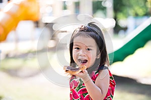 Portrait Asian cute kid eating bread with chocolate in playground outdoors. Snacks for kid when playing and exercising until her