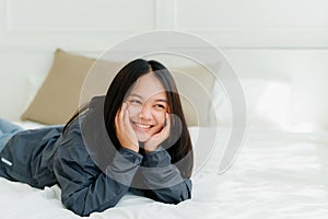 Portrait Asian cute long-haired teen wearing a gray long sleeve shirt Lay back and relax in bed in the bedroom happily.