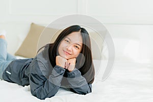 Portrait Asian cute long-haired teen wearing a gray long sleeve shirt Lay back and relax in bed in the bedroom happily
