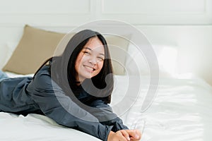 Portrait Asian cute long-haired teen wearing a gray long sleeve shirt Lay back and relax in bed in the bedroom happily