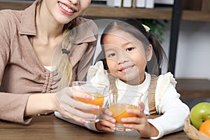 Portrait of Asian daughter girl child drinking fresh orange juice with mother during sitting in living room at home, parent take