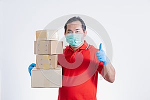Portrait of Asian delivery man with face medical mask in red cloth holding a box package.