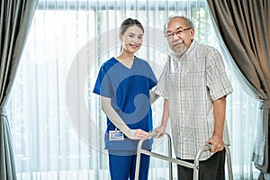 Portrait of Asian disabled Senior Elderly male stand with walker enjoy stay home nursing care. Beautiful nurse caregiver woman bes