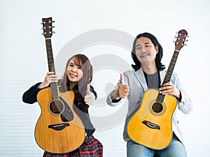 Portrait of Asian duo artists with an acoustic guitar sitting on a white background and show the gesture of thumps up for music,