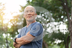 Portrait of Asian Elderly man with arms crossed relaxing over nature background. Happy confident Senior person in blue shirt