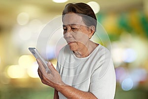 Portrait of asian elderly woman smiling with using mobile phone and colorful bokeh background