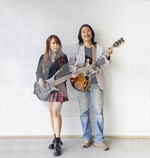 Portrait of Asian family duo rock band of young girl idol on bassist and male on semi hollow electric guitar standing on white