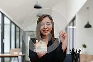 Portrait of an Asian female bank employee handing over a house and keys to a client after signing a contract on