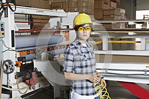 Portrait of an Asian female industrial worker with holding wire with machinery in background