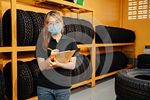 Portrait of asian female worker wear a mask to prevent the spread of corona virus or COVID-19 checking the stock of car tires at photo