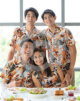 Portrait of Asian fun lovely family including senior dad beautiful mom sitting on chair and two handsome sons stand behind wearing