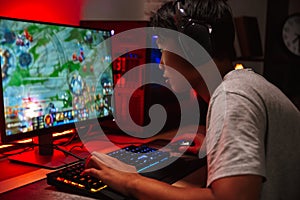 Portrait of asian gamer boy playing video games on computer in d