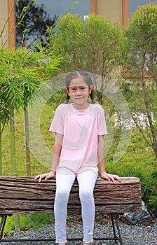 Portrait of Asian girl child looking camera while sitting on wooden bench in the garden