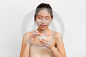 Portrait of Asian girl with cream on cheek holding jar