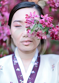 Portrait of Asian girl with her eyes closed, standing in front of a branch of cherry blossom that cover her face. The concept of a