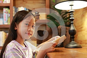 Portrait of Asian girl kid in casual clothes reading a book and smiling on the desk in the room