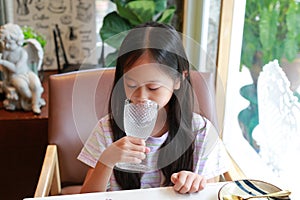 Portrait of Asian girl kid drinking water from glass while sitting at restaurant