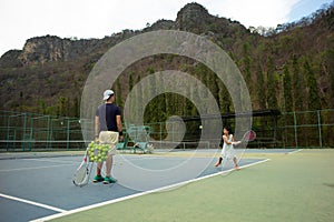 Portrait Asian girl plays tennis with her father and coach at outdoor court with stone mountain and forest background