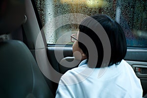 Portrait Asian girl sitting in car and looking out of window watching the rain.