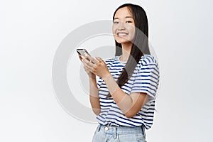 Portrait of asian girl using smartphone and smiling at camera, concept of cellular technology and mobile applications