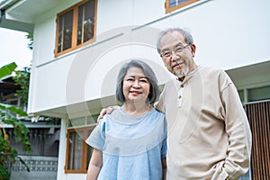 Portrait of Asian happy Senior elderly couple stand outdoor at house enjoy retirement life together. Loving Older grandparent hug