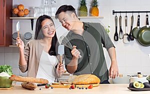 Portrait Asian happy young adult couple lover helping together, holding kitchenware, cooking in cozy home kitchen in morning,