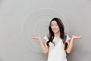 Portrait of asian indecisive woman with dark curly hair shrugging and throwing hands aside with clueless, isolated over gray back