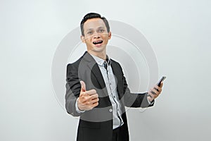 portrait of asian indonesian business man in suit holding smart phone with smlie and thumb up finger gesture on isolated