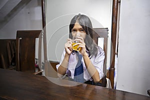 Portrait of Asian junior high school student girl in uniform breakfast with drinking orange juice in the morning