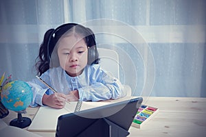 Portrait Asian kid girl wearing headphones looking at the tablet for learning education distance from home