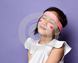 Portrait of asian Korean kid little girl with red hearts sign on cheek posing with closed eyes feeling bliss