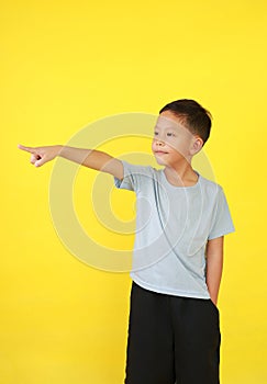 Portrait of Asian little boy child pointing index finger or forefinger and looking beside while standing isolated on yellow