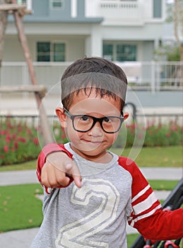 Portrait of Asian little boy child pointing straight at you and wearing glasses while stay in the garden