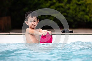 Portrait of asian little boy looking at camera and smiling while playing water in the swimming pool.