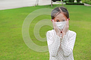 Portrait of Asian little girl kid wearing medical mask and touching on cheeks for protect covid-19 while stay in the garden