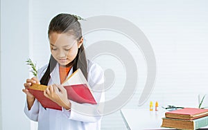 Portrait Asian little girl wearing white ground uniform, studying Science in class room at school, smiling, reading books, report