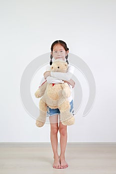 Portrait asian little kid girl hugging a teddy bear doll standing in white room