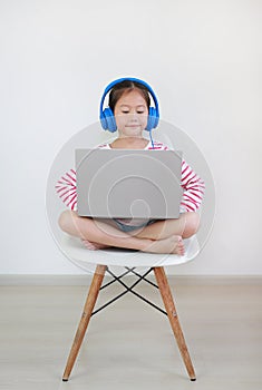 Portrait asian little school girl sitting on chair using headphone study online learning class by laptop computer during new