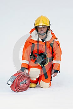 An Asian male firefighter in red protective uniform, mask and helmet with fire extinguisher sitting on white background.