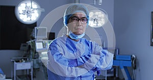 Portrait of asian male surgeon wearing lowered face mask, crossing arms in operating theatre